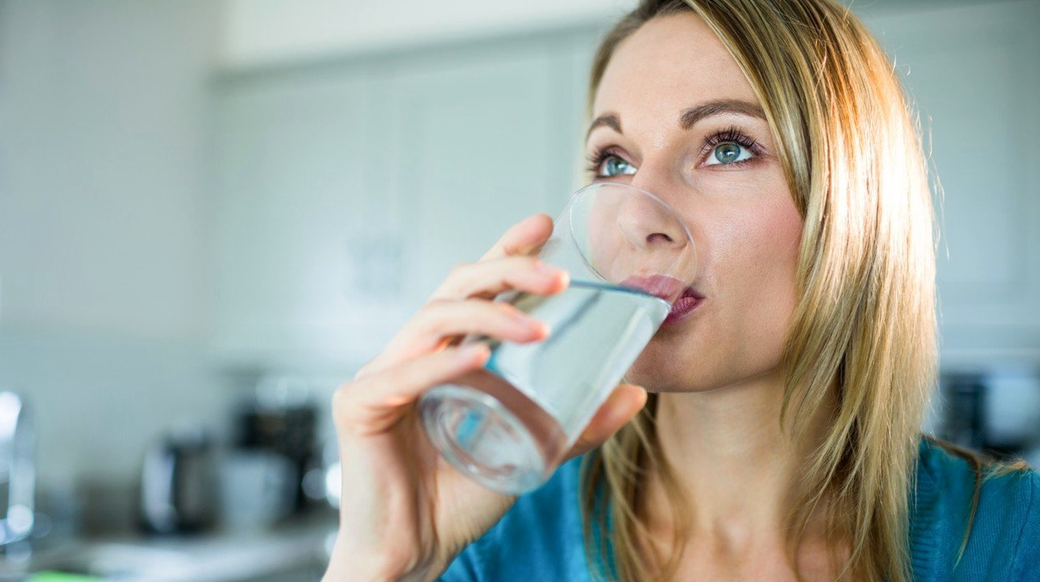 Feature | Pretty blonde woman drinking a glass of water at home | Why You Should Drink Hydrogen Water Instead of Purified Water